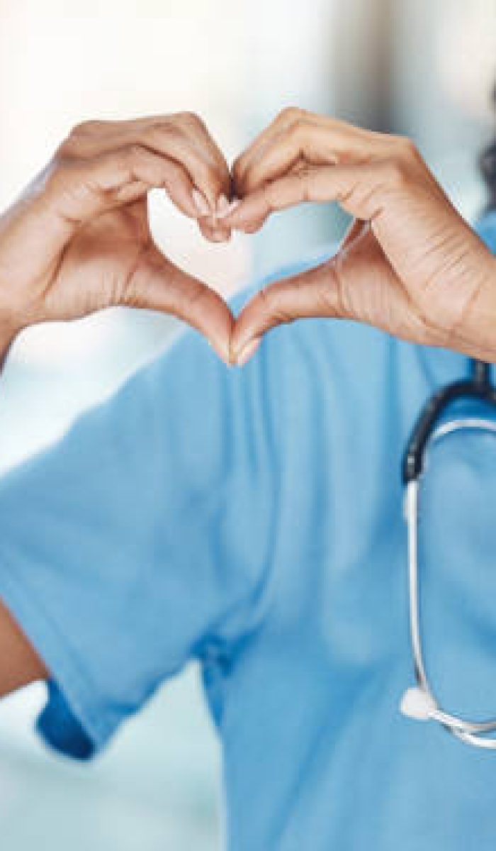 istockphoto-1400388878-612×612 Closeup african american woman nurse making a heart shape with her hands while smiling and standing in hospital. Take care of your heart and love your body. Health and safety in the field of medicine